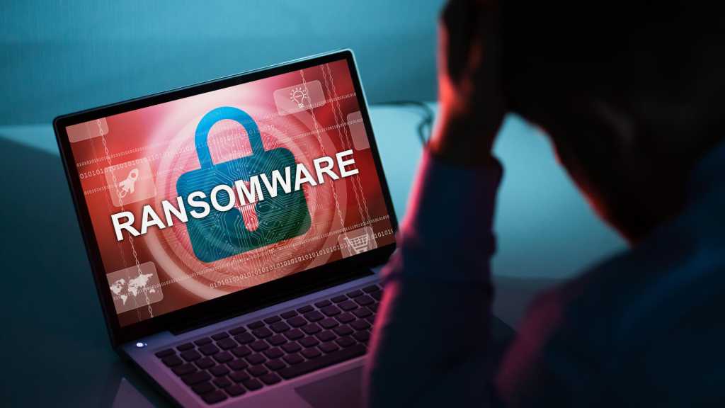 Ransomware auf Laptop-Bildschirm, verzweifelter Mensch sitzt davor